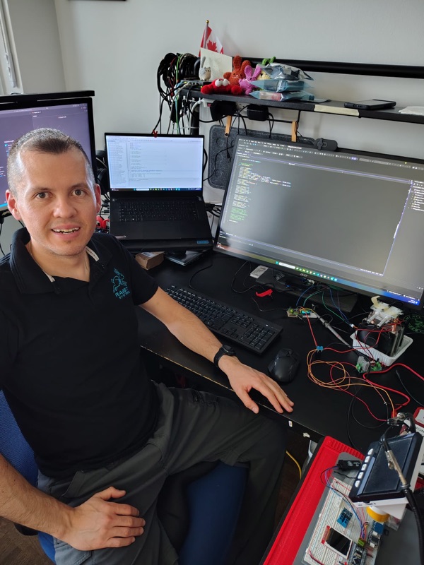 Carlos Narvaez at his workbench, surrounded by embedded systems prototypes, oscilloscope probes, and development boards.